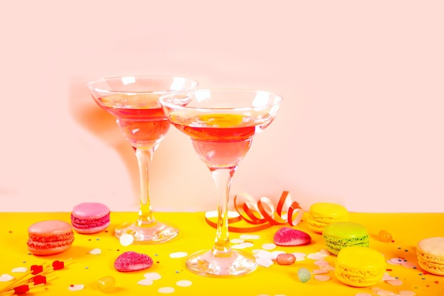 Glasses of pink cocktails with heart candies on yellow table Birthday party or Valentines day concept