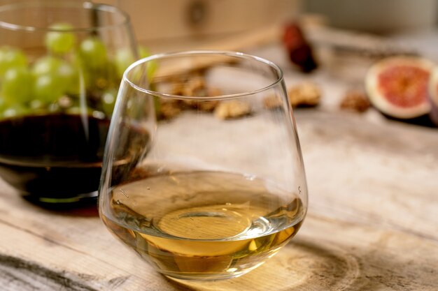 Glasses of red and white wine with grapes, figs, goat cheese and walnuts over old wooden background. Close up