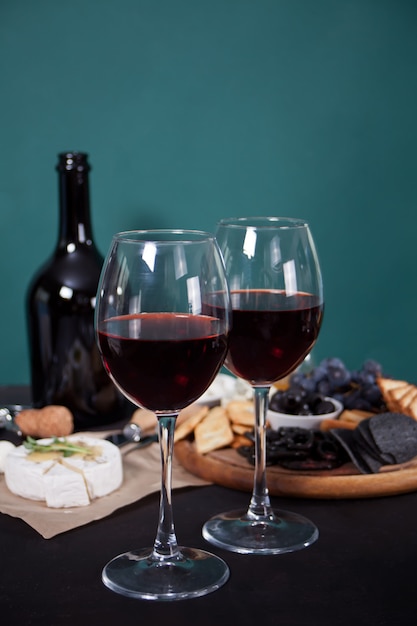 Glasses of red wine and plate with assorted cheese, fruit