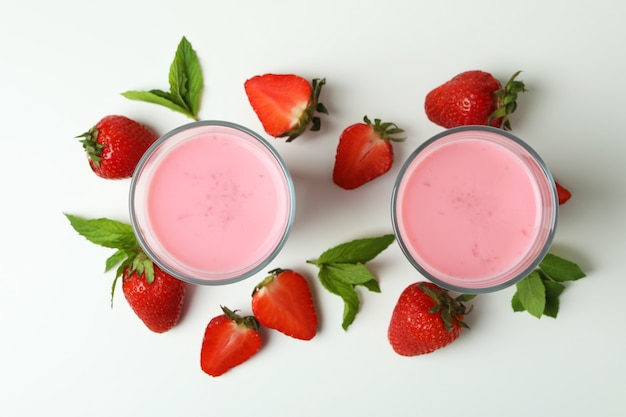 Glasses of strawberry milkshake and ingredients on white background