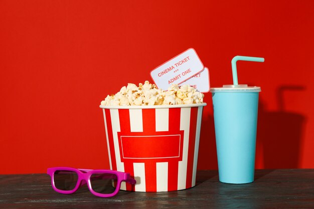 glasses, striped bucket with popcorn and tickets, paper cup against red background