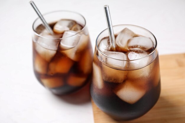 glasses of tasty cola with ice cubes on white table closeup