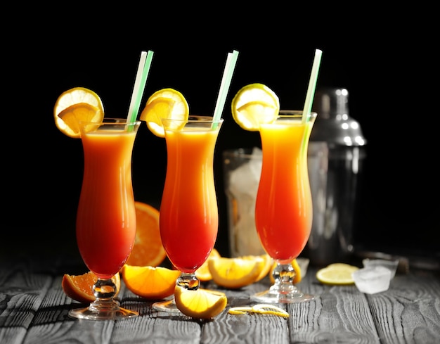 Glasses of Tequila Sunrise cocktail with citrus slices on dark background