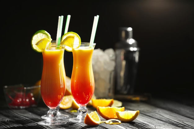 Бокалы коктейля Tequila Sunrise с кусочками цитрусовых на темном фоне