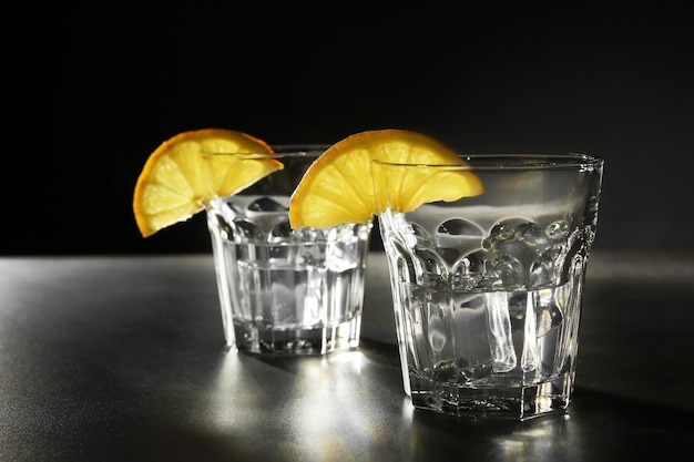 Glasses of vodka with lemon and ice on dark background