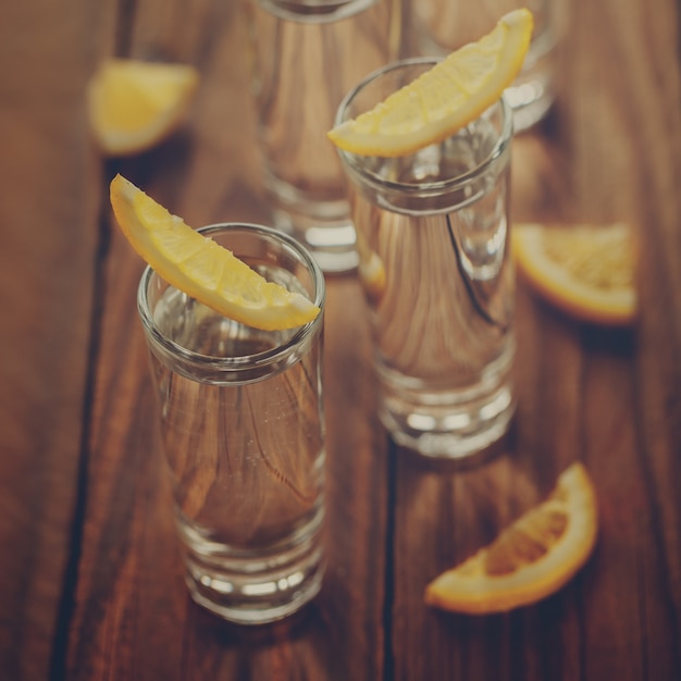 Glasses of vodka with lemon on wooden background. Toning image.