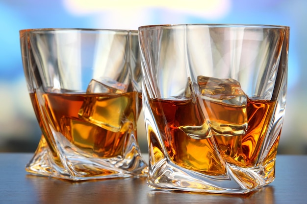 Glasses of whiskey on bright background