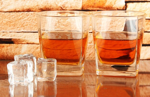 Photo glasses of whiskey and ice on brick wall background