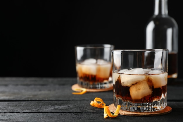 Glasses of whiskey with orange peels and ice on wooden