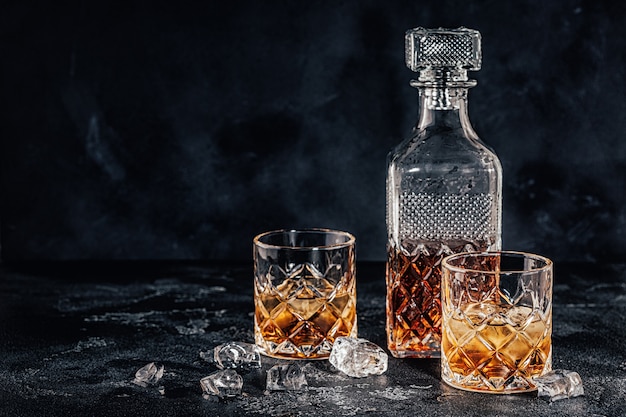 Glasses of the whiskey with a square decanter on a black stone background.