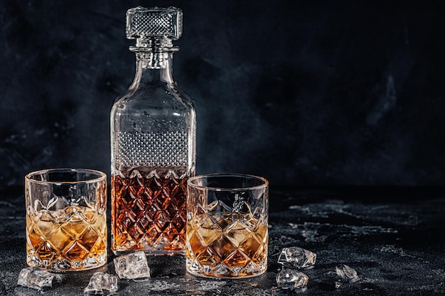 Glasses of the whiskey with a square decanter on a black stone background.