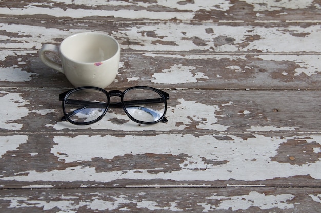 Очки и белая чашка на старом деревянном столе