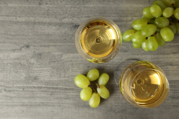 Glasses of white wine and grape on gray textured table