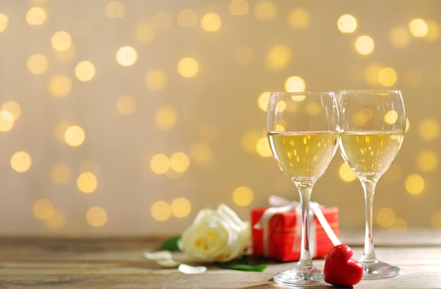 Glasses of wine, white roses and a gift in the box, on blurred background