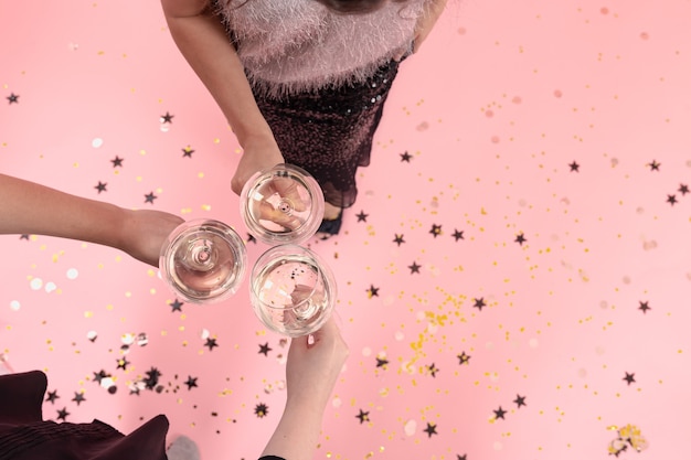 Glasses with champagne in the hands of girls at a party on a pink background, copy space.