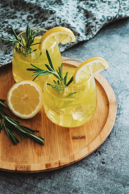 Foto bicchieri di limonata fredda a cocktail a fette di limone e pianta di rosmarino sul tavolo di cemento