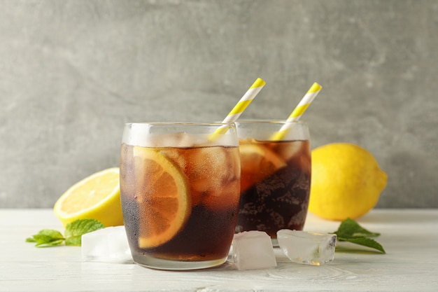 Glasses with cold cola and citrus on white cement background, space for text