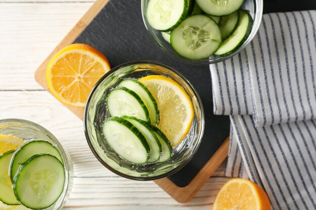 Glasses with cucumber water on board on wood background, top view