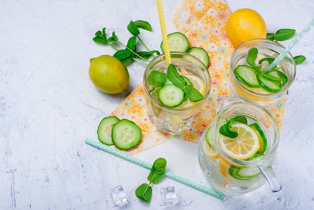 Glasses with detox fresh organic cucumber, lemonnd mint water on white table 