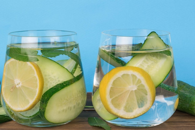 Glasses with a drink of lemon and cucumbers on a wooden table on a blue background