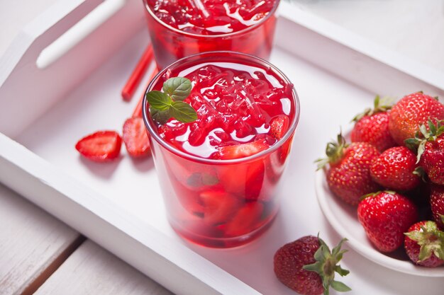 Glasses with fresh homemade strawberry sweet iced tea or cocktail, lemonade with mint. Refreshing cold drink and plate with strawberry on the wooden white tray.