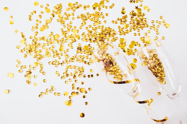 Glasses with golden confetti tinsel on white background. Flat lay, top view, copy space. Celebrate party concept