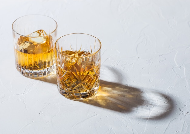 Glasses with ice cubes of single malt whiskey on white background with deep shadow.