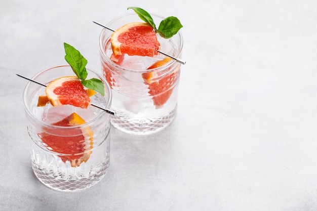 Фото Очки с коктейлем из красного грейпфрута с кусочком фруктов на сером фоне