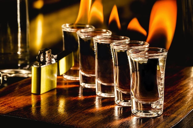 Glasses with tequila shots on fire, flaming drink, bar setting