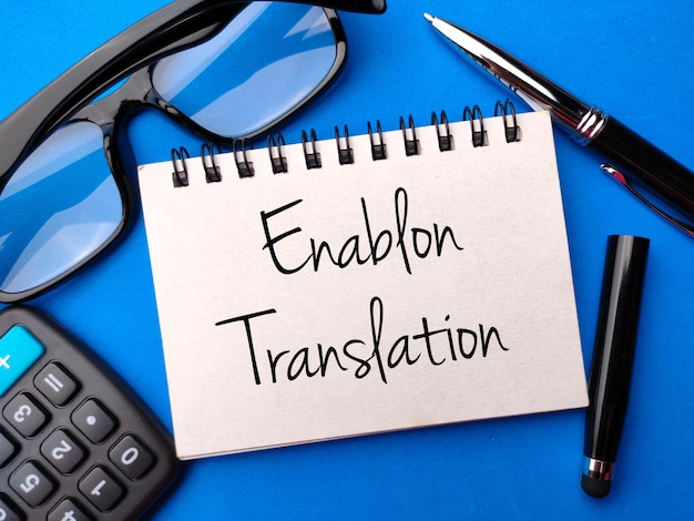 メガネ電卓ペンと青色の背景に Enablon Translation のテキストが記載されたノート