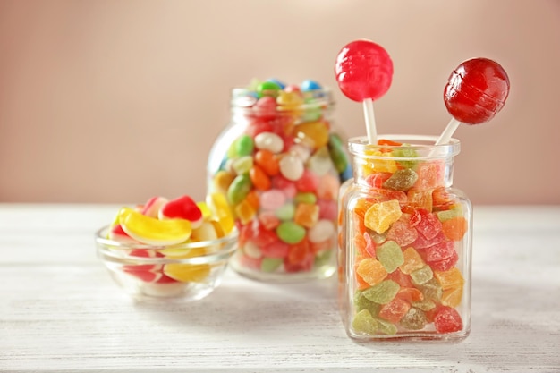 Стеклянная посуда с разноцветными конфетами и сахаром на столе на светлом фоне