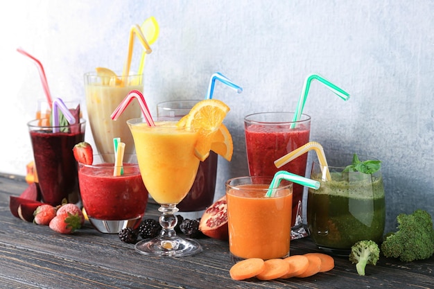 Glassware with different smoothies on table against light background