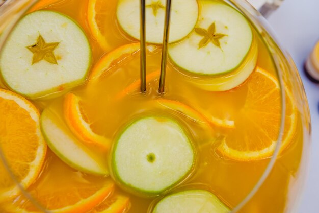 Glassware with refreshing citrus fruits cocktail Lemonade with fresh slices of oranges lemons and apples in glass Closeup