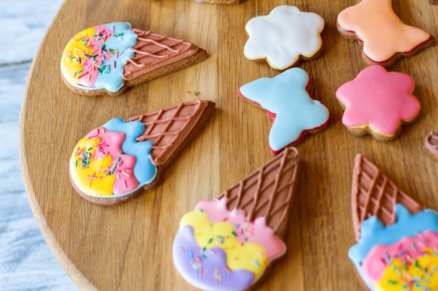 Glazed cookies on wooden board. Biscuits shaped as flowers. Desserts for home party. Sugar frosting and crispy dough.