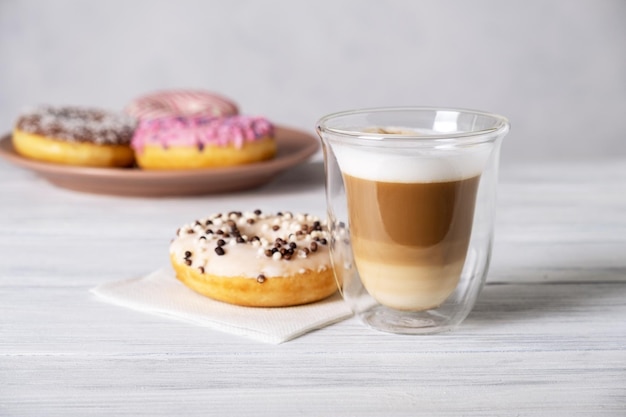 Glazed decorated donuts on plates and coffee latte or cappuccino with milk foam in a heatresistant glass cup Selective focus