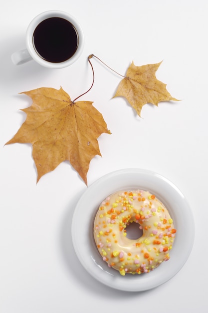 Glazed donut with sprinkles, cup of coffee and autumn leaves