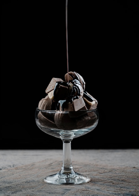 Glazen beker gevuld met chocolaatjes druipende chocoladesiroop