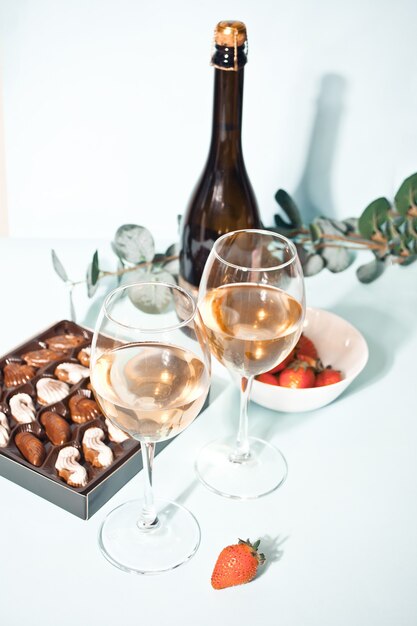 Glazen champagne of witte druivenwijn met plaat van chocolade en aardbei, fles op de achtergrond.