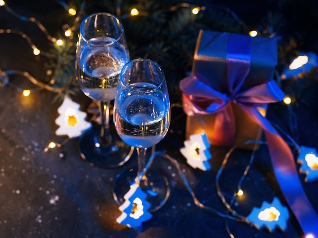 Glazen champagne op de kersttafel 's nachts. lichtgevende slinger, geschenken en takken van de kerstboom. kerst achtergrond