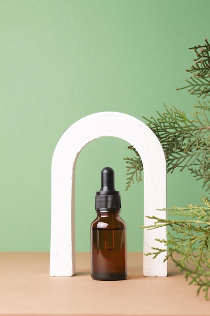 Glazen druppelflesje met essentiële cosmetische olie of serum in boog met thuja-takken Hyaluronzuur-olieserum met collageen en peptiden huidverzorgingsproduct