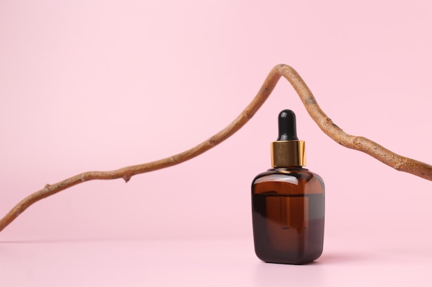 Glazen druppelflesje met essentiële cosmetische olie of serum op pastelkleurige achtergrond met takboom Kruiden homeopathische producten Natuurlijke organische spa-cosmetica