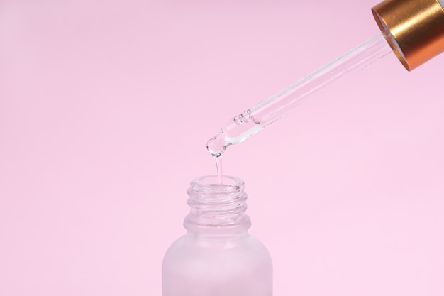 Glazen druppelflesje met olieachtige druppel valt uit cosmetische pipet