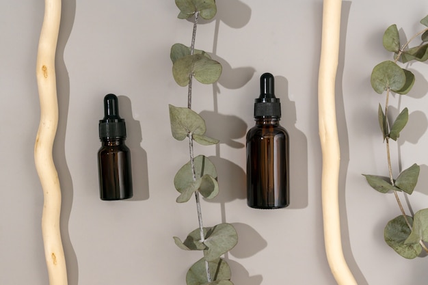 Glazen druppelflesjes met eucalyptusolie. trendy biologische cosmetica, anti-verouderingsolie voor het gezicht. stillevensamenstelling met eucalyptusbladeren op grijze achtergrond met houten stokken.