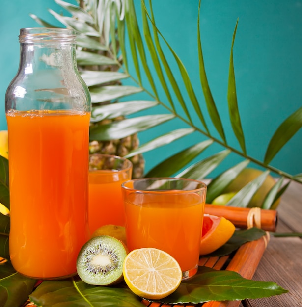 Glazen en fles tropisch exotisch multifruitsap met ananas en palmblad op de achtergrond