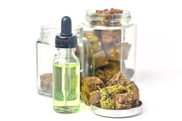 Glazen fles cannabisolie en een pot gedroogde cannabis op een witte achtergrond CBD-hennepoliehennepolie Medische marihuanaproducten, waaronder cannabisblad cbd en hasjolie alternatieve geneeskunde