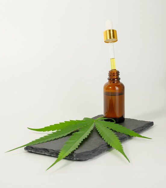 Glazen fles CBD olie cannabis extract marihuanablad op zwarte steen, medisch kruid concept.