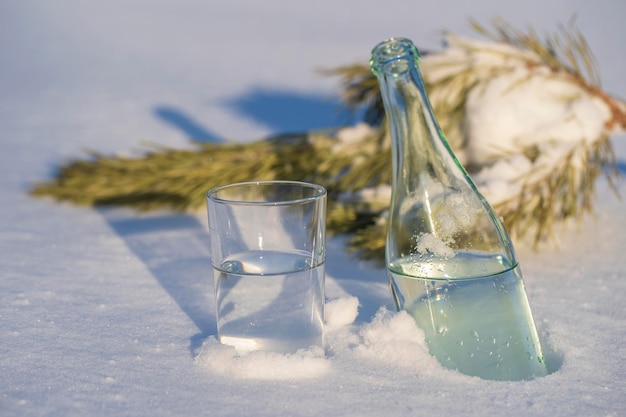 Glazen fles en glas water op een witte sneeuw in de winter