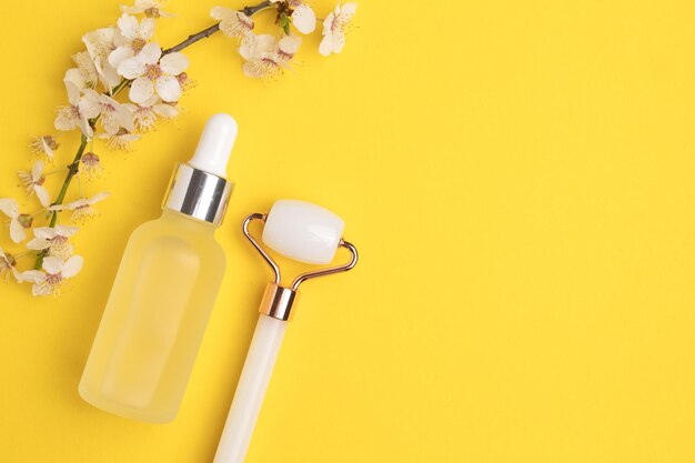 Glazen fles met olie-gezichtsroller voor gezichtsmassage op een gele achtergrond met bloeiende kersen Cosmetische gezichtsverzorging en spa Natuurlijk behandelingsconcept