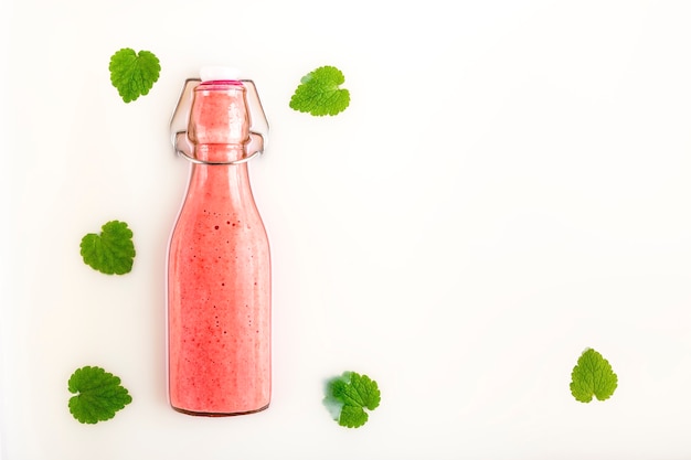 Glazen fles met verfrissende roze aardbeiensmoothie over melk met groene bladeren en kopieerruimte. Gezond, detox en dieetvoedselconcept.