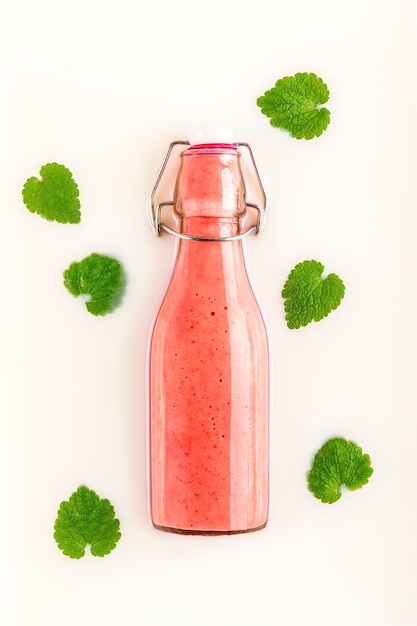 Glazen fles met verfrissende roze aardbeiensmoothie over melk met groene bladeren. Gezond, detox en dieetvoedselconcept.